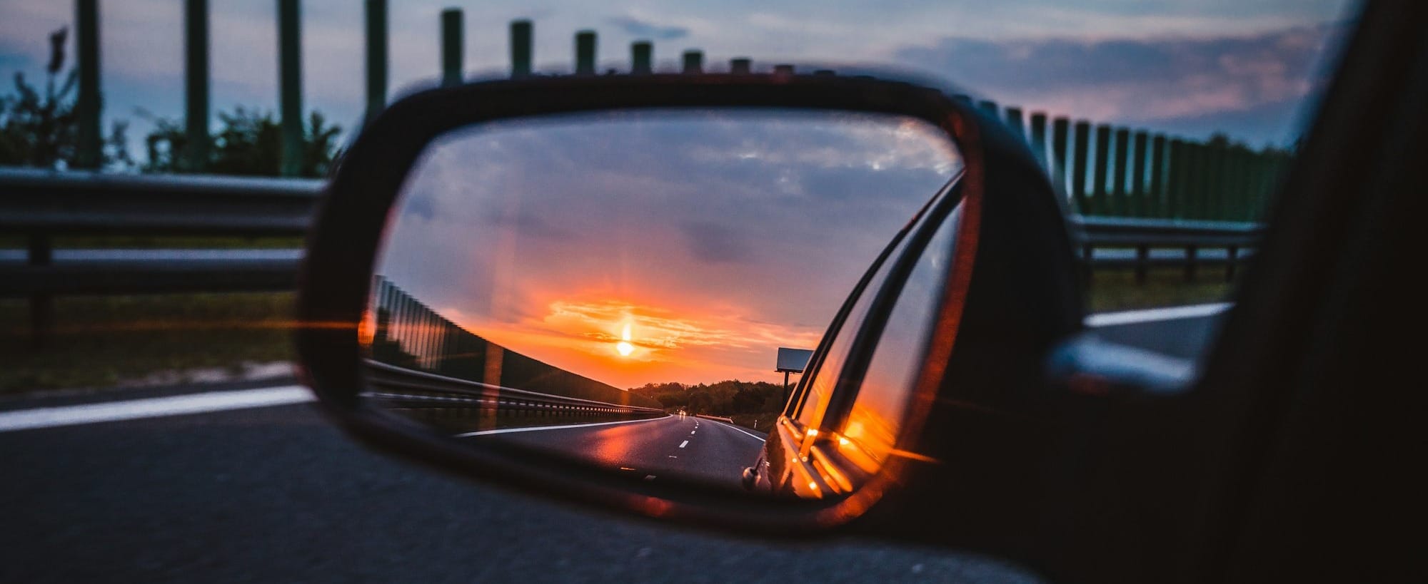 a rear view mirror reflecting a sunset in the side view mirror