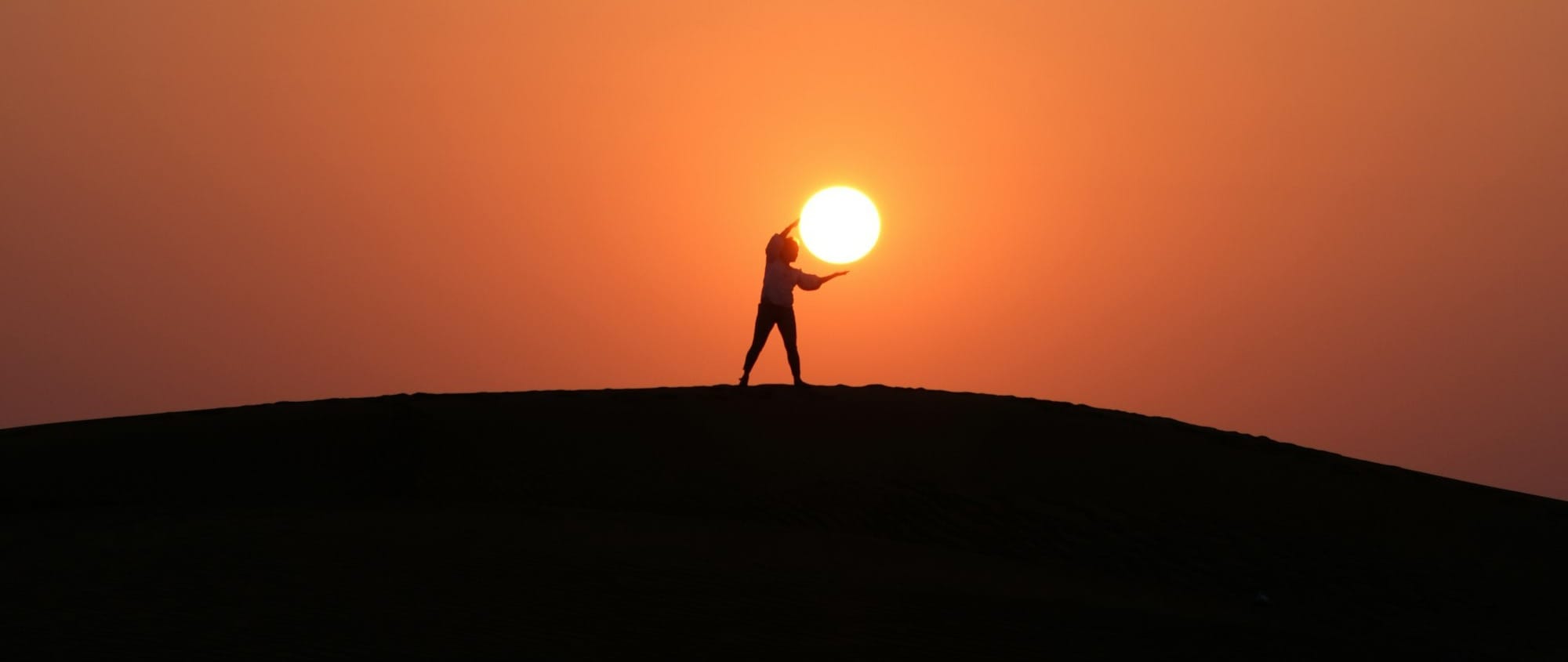 silhouette of person standing on hill during sunset